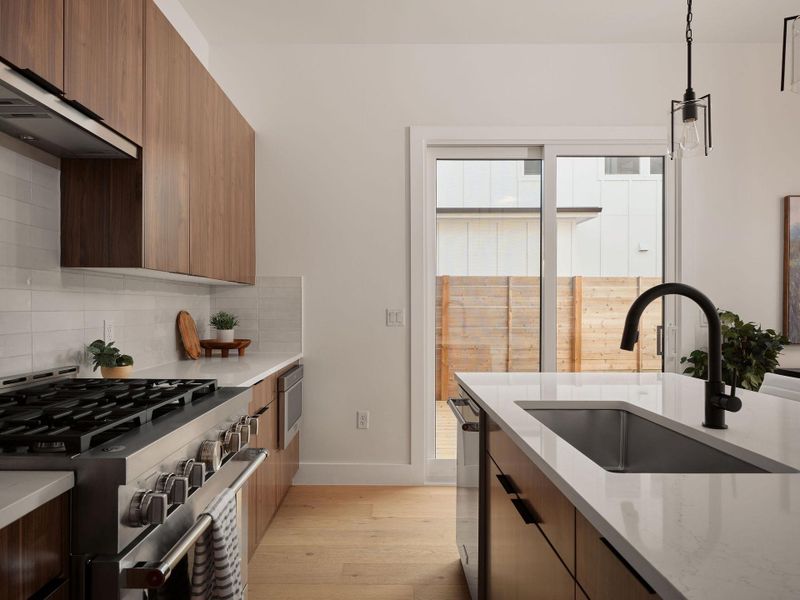 Kitchen featuring brown cabinetry, modern cabinets, light wood finished floors, appliances with stainless steel finishes, and decorative light fixtures Kitchen featuring brown cabinetry, modern cabinets, light wood finished floors, appliances with stainless steel finishes, and decorative light fixtures