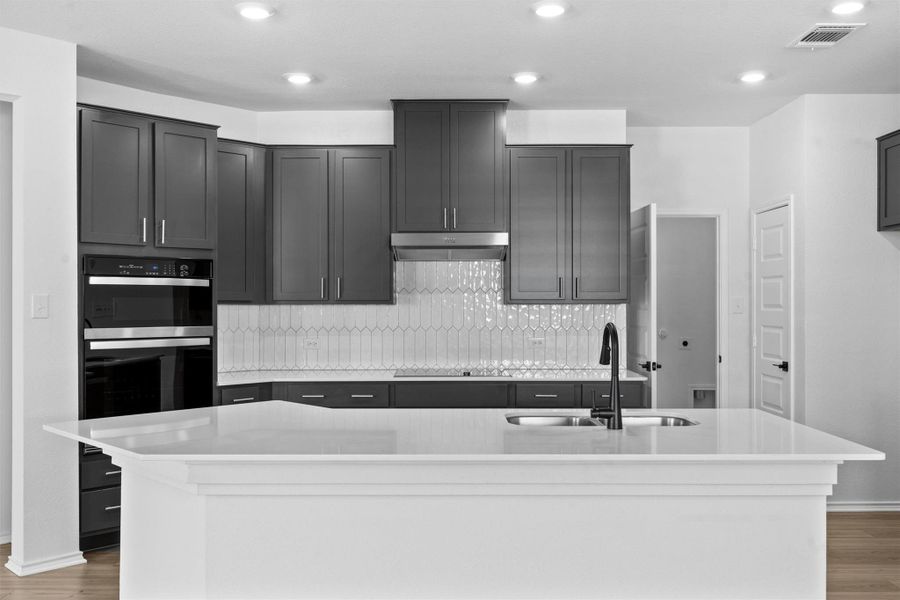 Kitchen with light wood-style floors, a center island with sink, light stone countertops, decorative backsplash, and recessed lighting