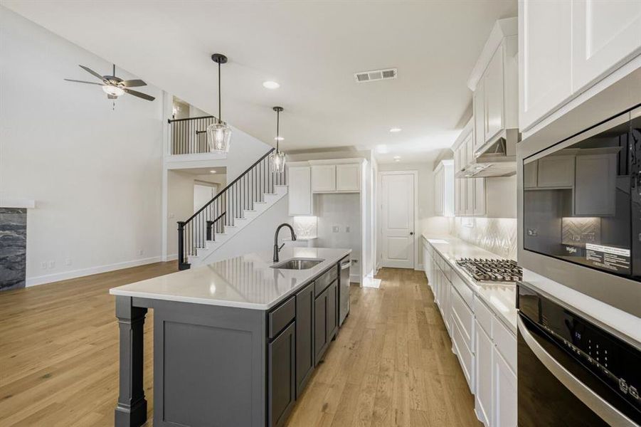 Two tone kitchen featuring dual tone cabinets, stainless steel appliances, a kitchen island with sink, light wood-style floors, and a kitchen breakfast bar