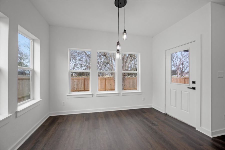 Bright room with large windows and dark hardwood floors, featuring a modern light fixture. Ideal for a dining area or sitting room, with a view of the fenced backyard. Bright room with large windows and dark hardwood floors, featuring a modern light fixture. Ideal for a dining area or sitting room, with a view of the fenced backyard.