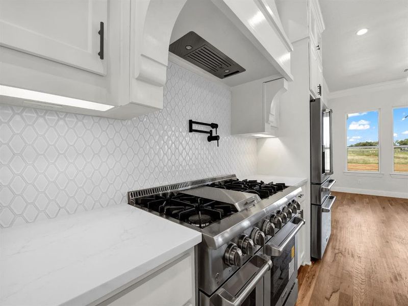 Kitchen with crown molding, appliances with stainless steel finishes, tasteful backsplash, light hardwood / wood-style floors, and white cabinetry