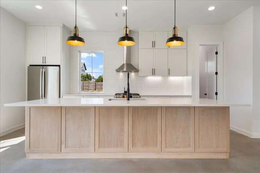Kitchen featuring finished concrete flooring, recessed lighting, an island with sink, freestanding refrigerator, and decorative light fixtures