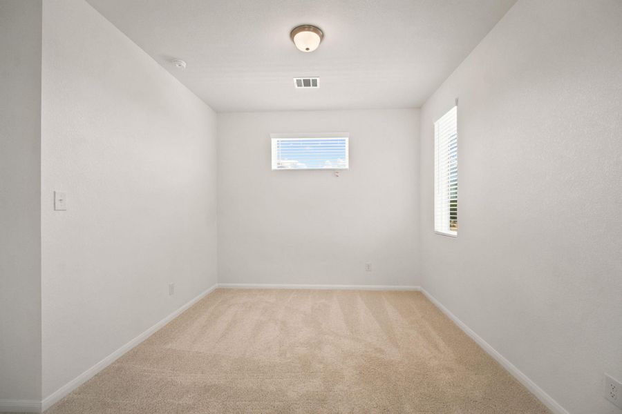 An airy secondary bedroom features plush neutral carpeting and dual windows that invite natural light.