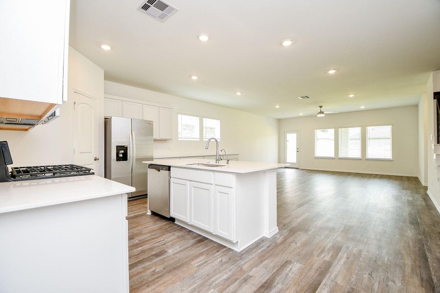 Bright and modern kitchen with white cabinetry, stainless steel appliances, and a large island with a sink. Features recessed lighting and wood-look flooring, providing a sleek and inviting space.