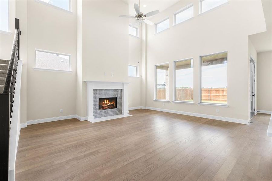 Unfurnished living room featuring light hardwood / wood-style floors, a tiled fireplace, ceiling fan, and a towering ceiling