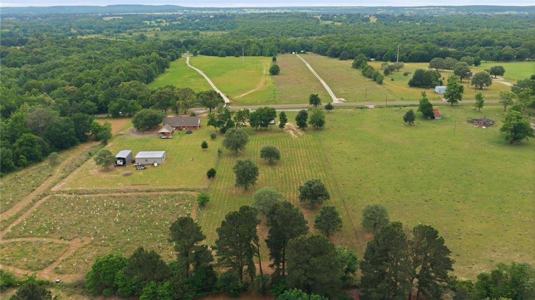 Expansive property featuring a main residence, two outbuildings, open fields, and wooded areas