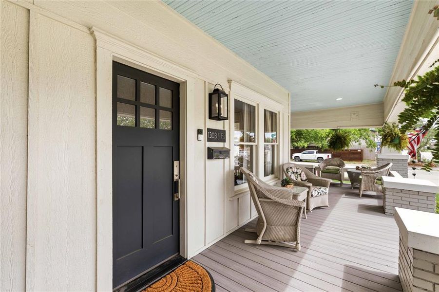 Inviting front porch featuring a dark paneled entry door with transom windows, board and batten siding, beadboard ceiling, and gray wood-finish decking