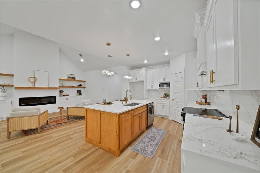 Kitchen with backsplash, light wood finished floors, lofted ceiling, light stone countertops, and white cabinetry