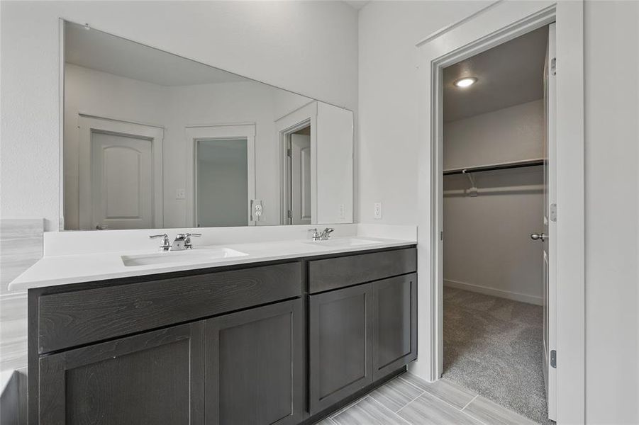 Full bathroom featuring double vanity, light colored carpet, and a spacious closet Full bathroom featuring double vanity, light colored carpet, and a spacious closet