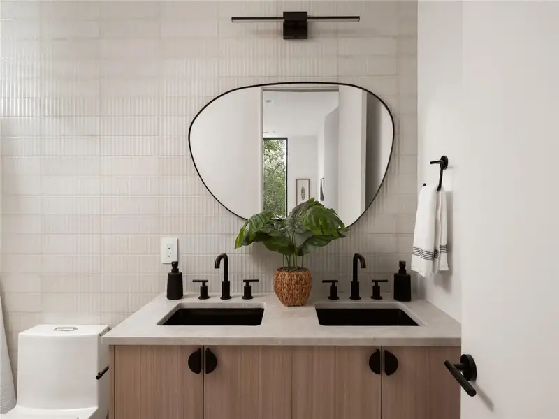A naturally illuminated en-suite second bathroom featuring a contemporary dual vanity and unique mirror. A naturally illuminated en-suite second bathroom featuring a contemporary dual vanity and unique mirror.
