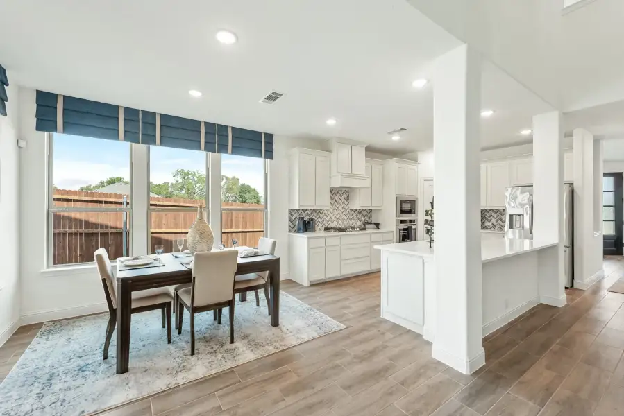 Open-plan dining area and kitchen with white cabinets, wood-look floors, and large windows