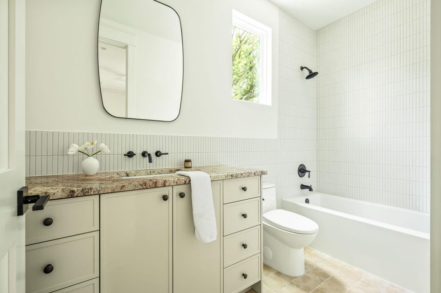 A pristine bathroom featuring a vanity with a stone counter, complemented by sleek dark fixtures and elegant tiled walls.