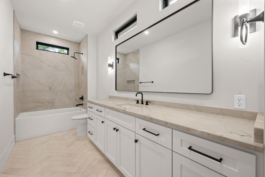 Elegant stone countertops and a modern bathtub define this meticulously finished space.