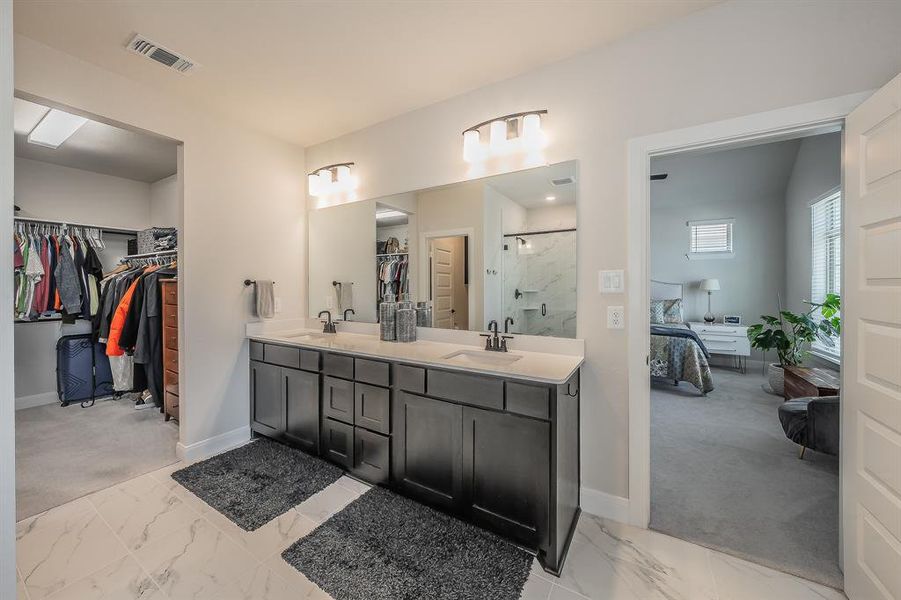 Full bathroom featuring ensuite bathroom, a marble finish shower, a spacious closet, double vanity, and light marble finish flooring