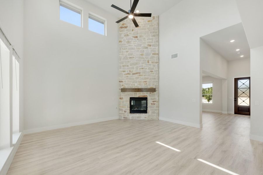 Open living room with floor-to-ceiling stone fireplace, high ceilings, ceiling fan, and light wood floors