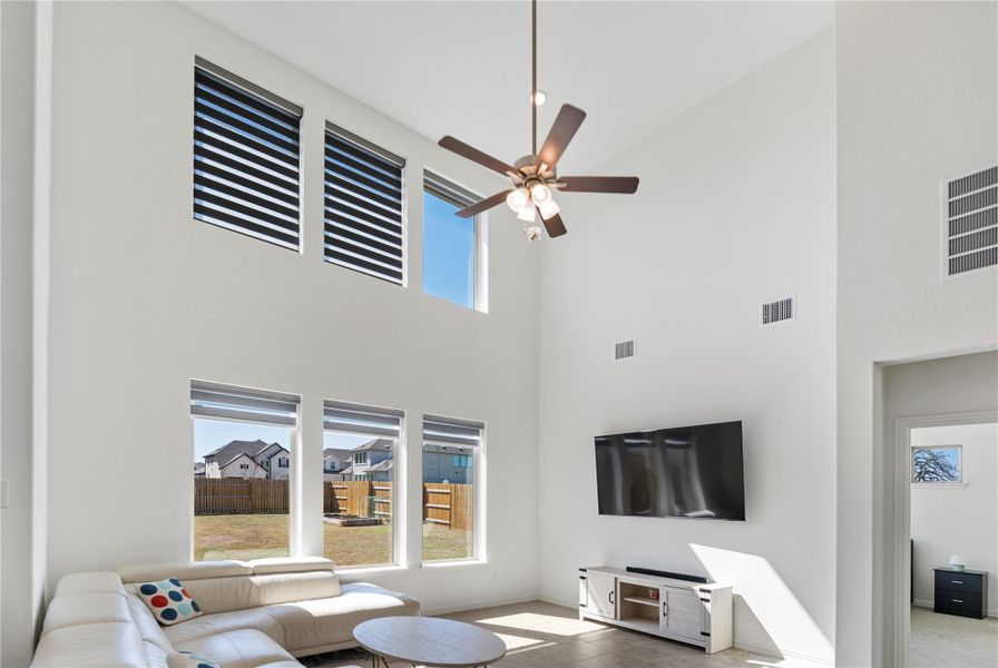 A living room with towering ceilings and multiple large windows illuminates a spacious interior. A living room with towering ceilings and multiple large windows illuminates a spacious interior.