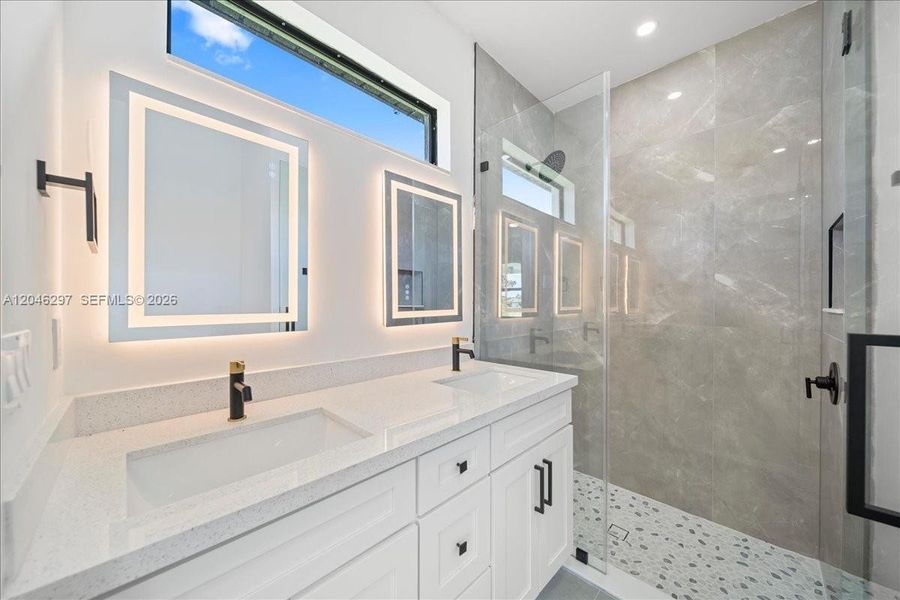 Spa-inspired bathroom featuring a dual-sink quartz vanity, illuminated designer mirrors Spa-inspired bathroom featuring a dual-sink quartz vanity, illuminated designer mirrors