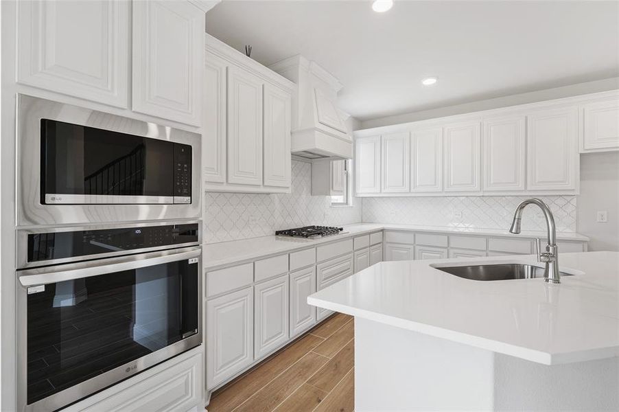 Kitchen with stainless steel appliances, white cabinetry, tasteful backsplash, wood tiled floors, and recessed lighting