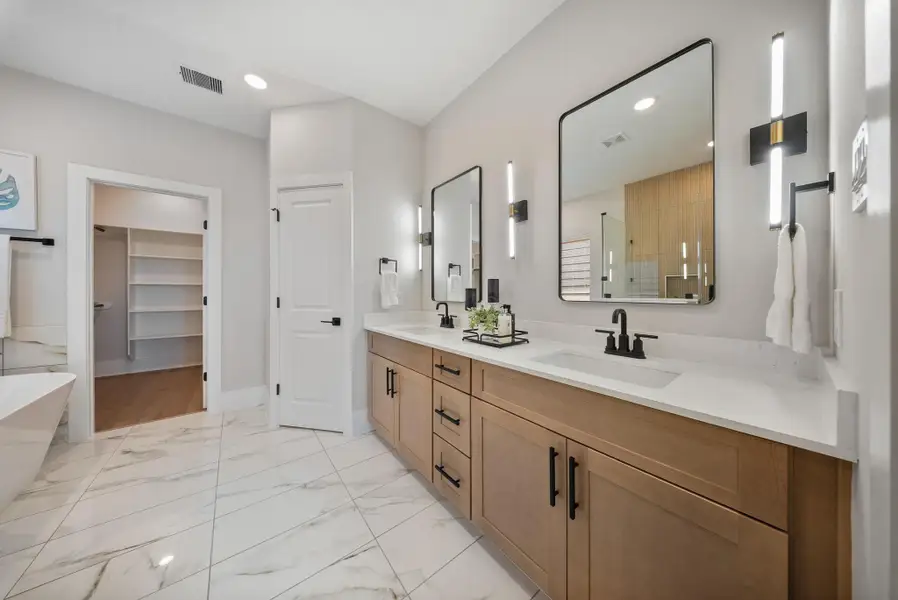 Luxurious master bathroom featuring elegant dual vanities, modern fixtures, and a spacious walk-in closet.