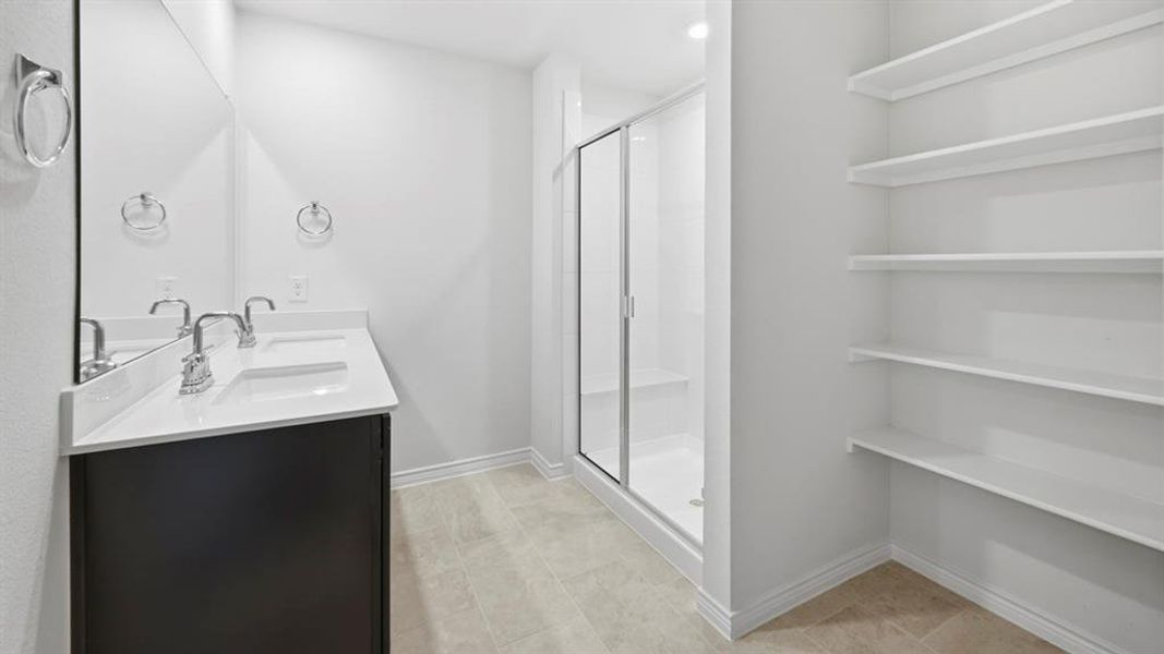 Bathroom featuring double vanity, a stall shower, and light tile patterned floors