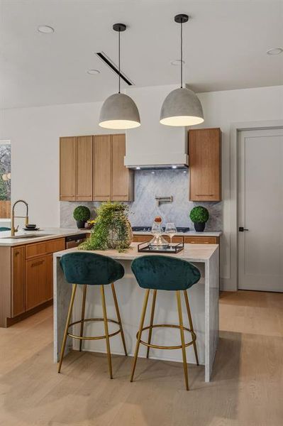 Kitchen with a center island, brown cabinetry, hanging light fixtures, and light stone countertops