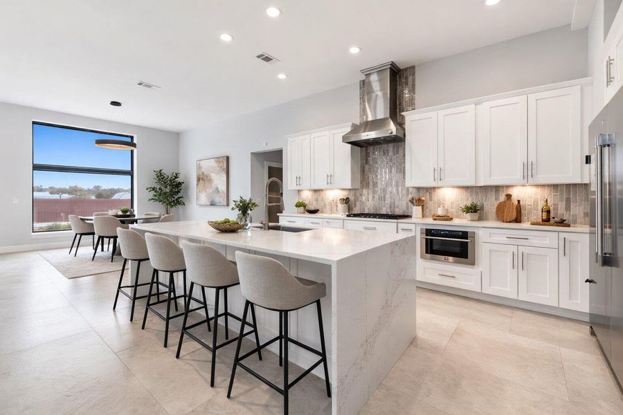 Kitchen with white cabinets, light stone counters, an island with sink, stainless steel appliances, and a kitchen breakfast bar
