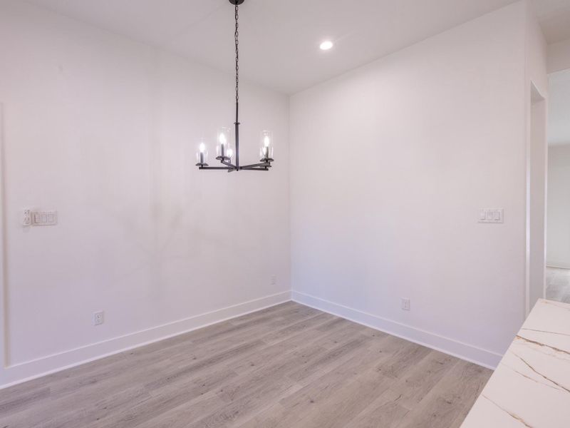 Bright dining area with light wood flooring and a modern black chandelier. The white walls and recessed lighting create a clean, spacious feel. Ideal for intimate gatherings.