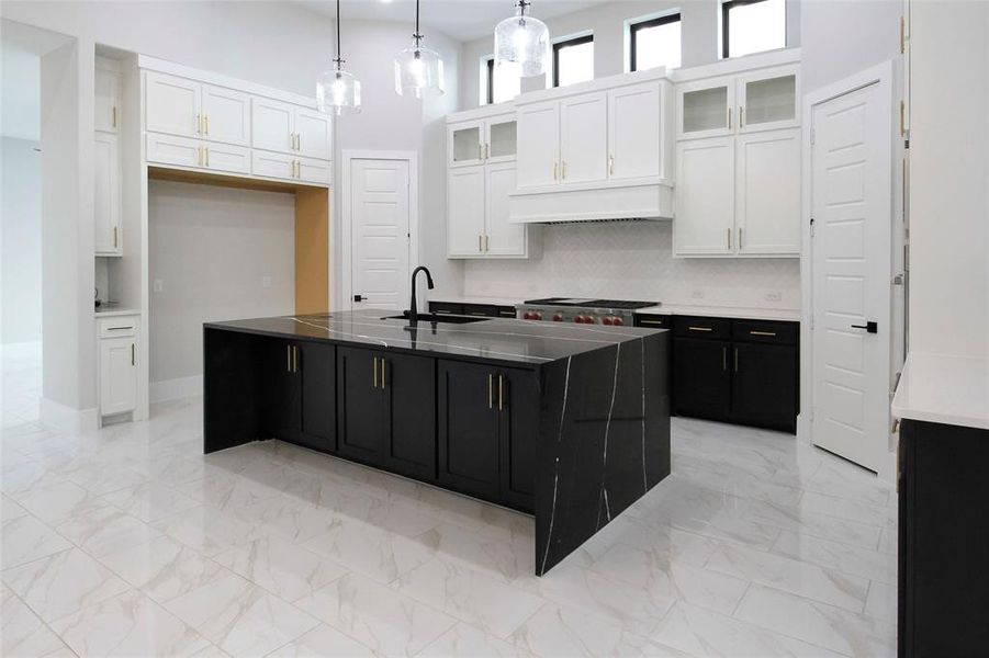 Kitchen with white cabinets, sink, an island with sink, and hanging light fixtures