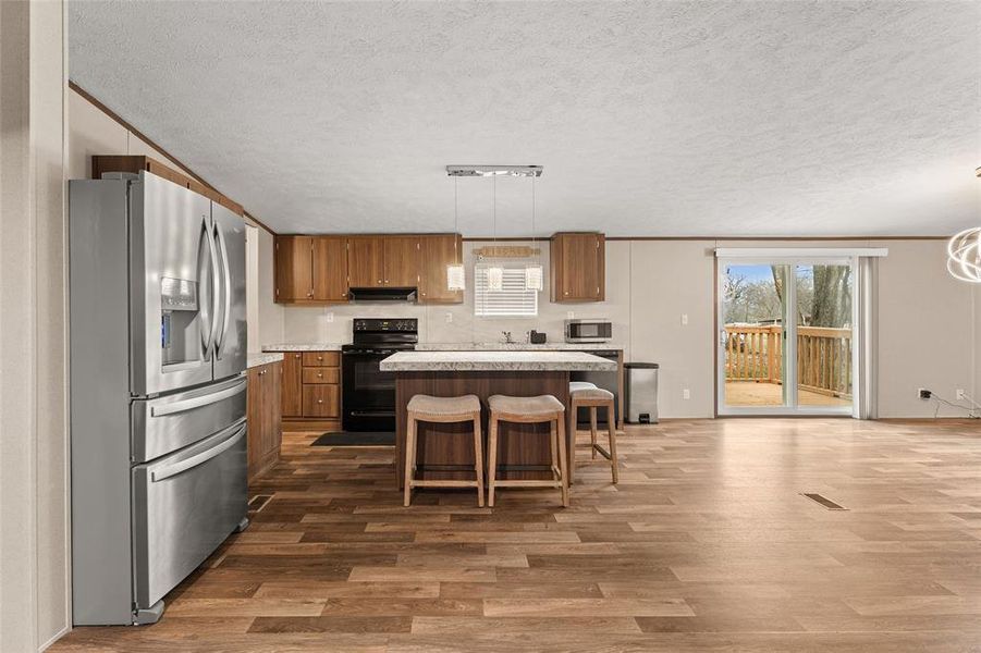 Kitchen with stainless steel appliances, light countertops, a center island, wood finish cabinetry, and plenty of natural light