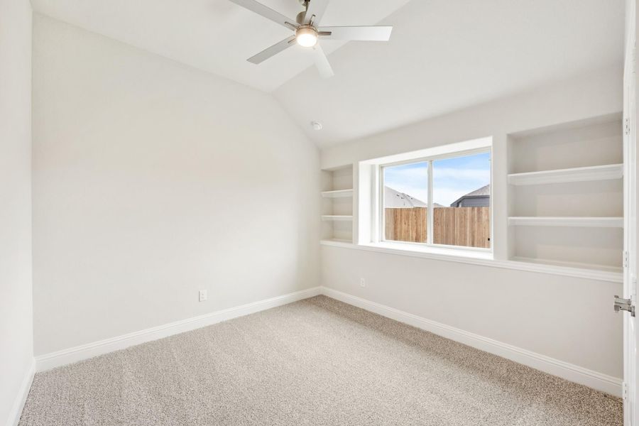 Empty bedroom with vaulted ceiling, ceiling fan, built-in shelves, and carpet flooring