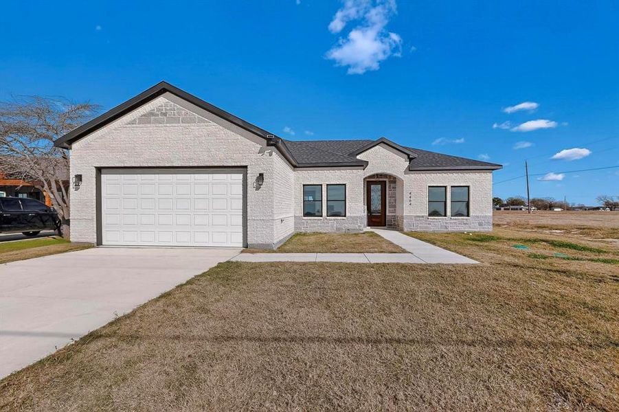 View of front facade featuring a front yard, driveway, an attached garage, and brick siding