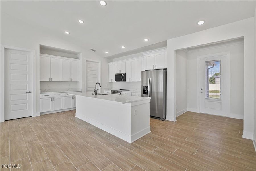 Kitchen featuring appliances with stainless steel finishes, white cabinets, vaulted ceiling, recessed lighting, and an island with sink
