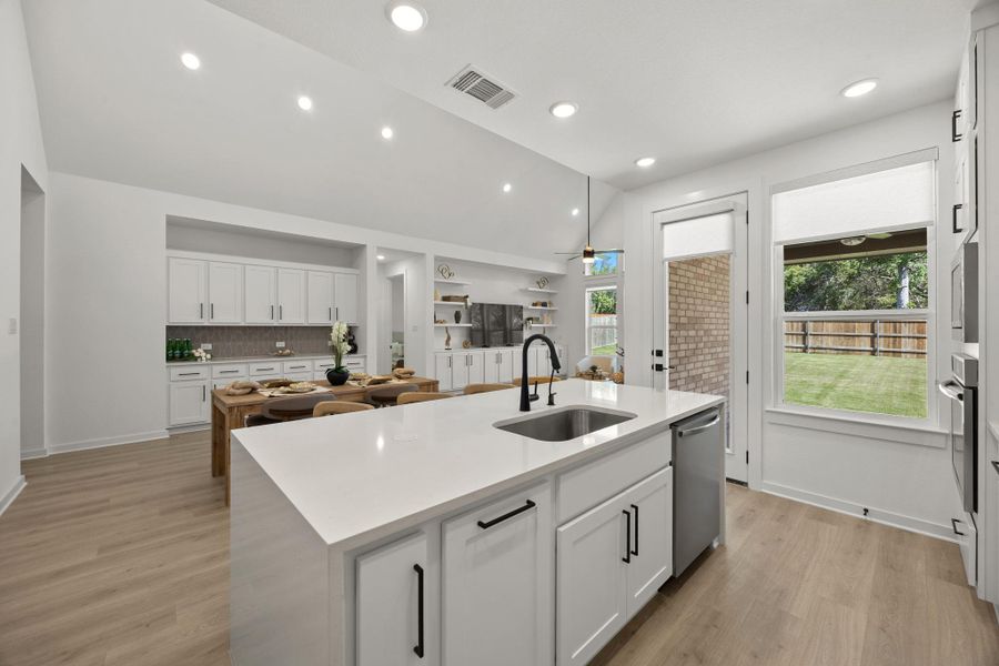 Kitchen with vaulted ceiling, white cabinets, a kitchen island with sink, light stone countertops, and light wood-type flooring