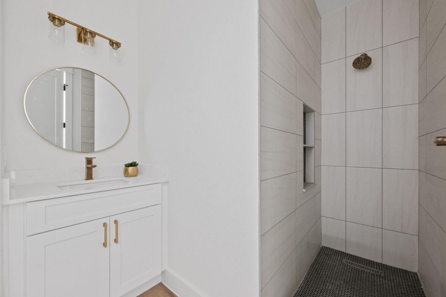 Bathroom featuring a shower with light-toned rectangular wall tiles and a dark circular floor tile pattern