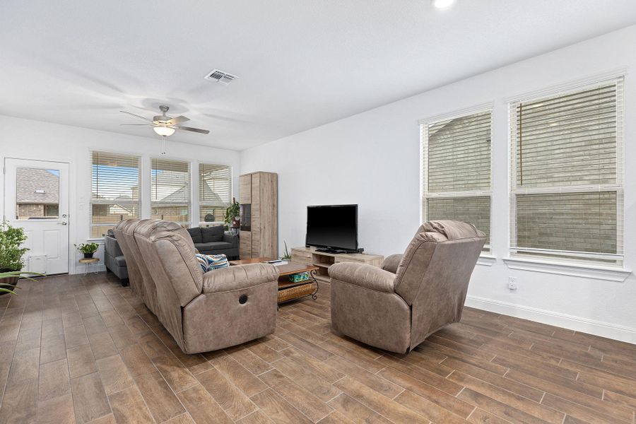 Rich wood-look flooring grounds this open living area, complemented by natural light and a modern ceiling fan.