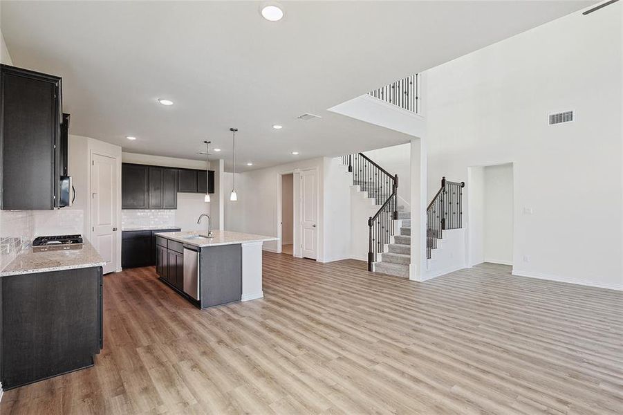 Kitchen featuring decorative light fixtures, wood-type flooring, sink, an island with sink, and decorative backsplash