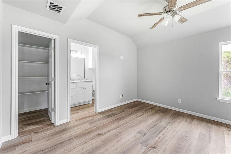 Unfurnished bedroom featuring lofted ceiling, a spacious closet, a closet, light wood finished floors, and baseboards Unfurnished bedroom featuring lofted ceiling, a spacious closet, a closet, light wood finished floors, and baseboards