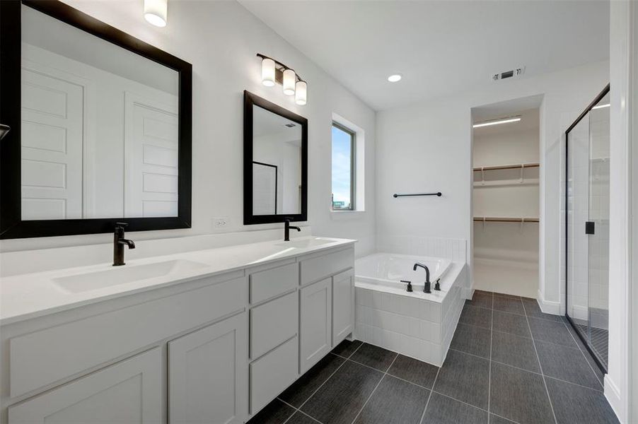 Bathroom featuring double vanity, a garden tub, a spacious closet, a stall shower, and dark tile patterned floors