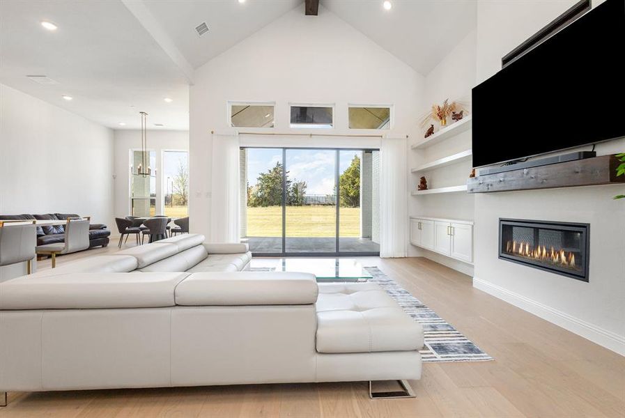 Living area featuring light wood-type flooring, a glass covered fireplace, high vaulted ceiling, recessed lighting, and a chandelier