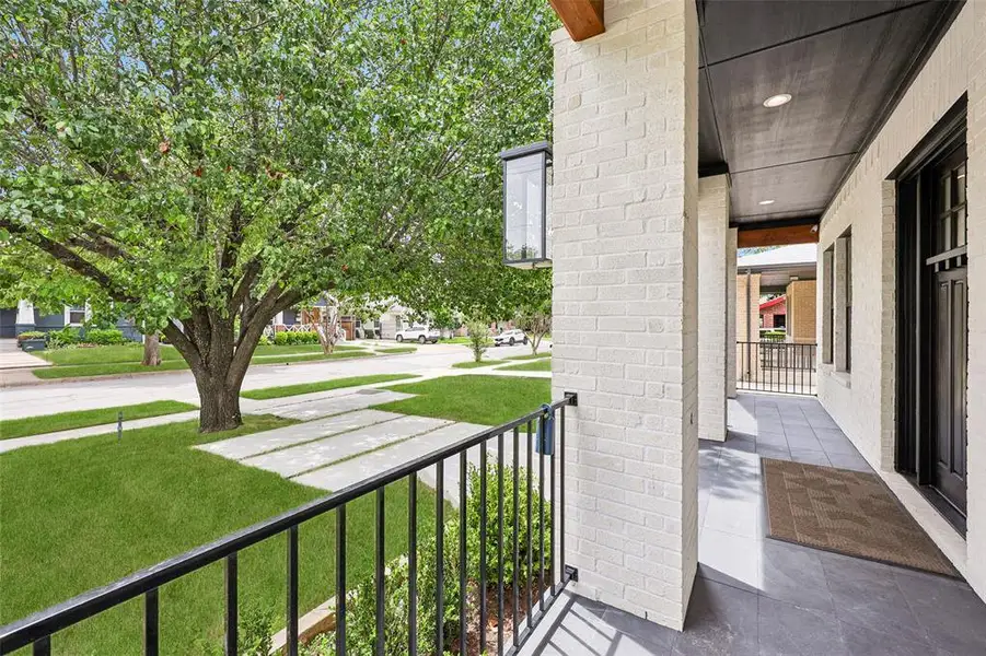 Covered front porch featuring light-colored brick facade, dark-toned ceiling, recessed lighting, and a black metal railing