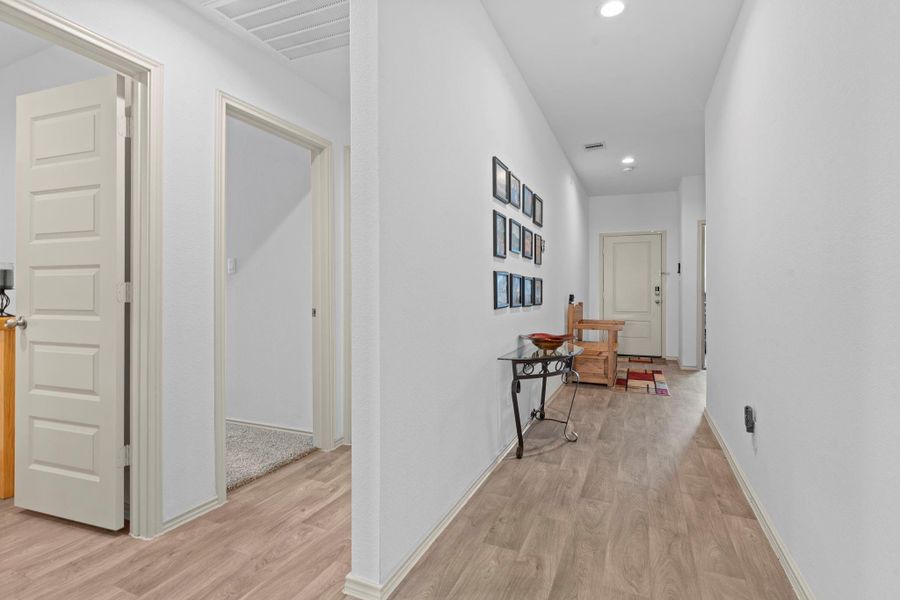 Long, light-filled hallway with durable wood-look vinyl floors and 5-panel shaker doors leading to secondary bedrooms and living areas while keeping everything connected yet private. The left hallway has a half bathroom and private guest bedroom. Long, light-filled hallway with durable wood-look vinyl floors and 5-panel shaker doors leading to secondary bedrooms and living areas while keeping everything connected yet private. The left hallway has a half bathroom and private guest bedroom.