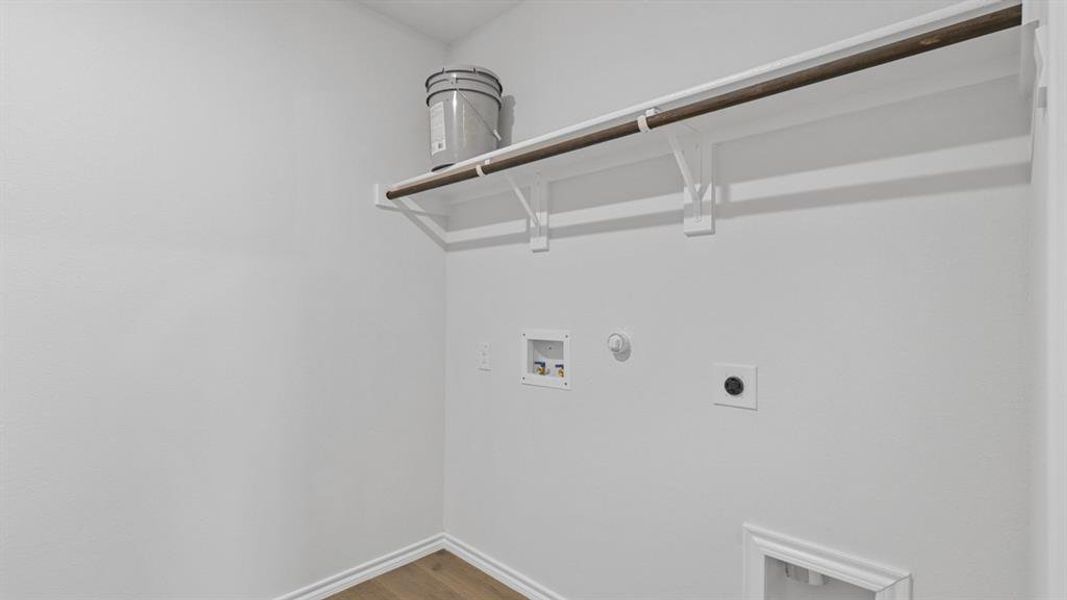 Utility area featuring wood-finish flooring, white painted walls, and an overhead storage shelf with an integrated hanging rod