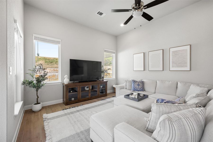 The spacious, light-filled living room features wood-finished flooring, recessed lighting, a ceiling fan, and window blinds—plus serene views of the outdoors that bring the beauty of nature inside.