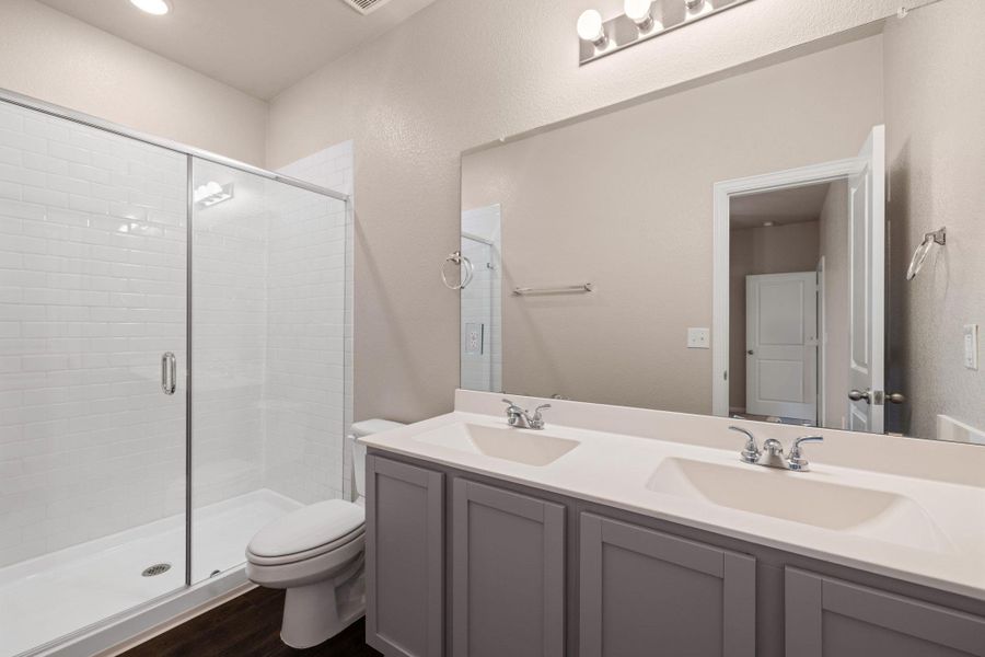 Full bathroom featuring double vanity, a stall shower, and dark wood-style flooring