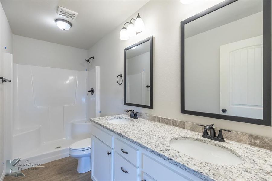 Bathroom with light wood-style floors, a shower stall, and double vanity