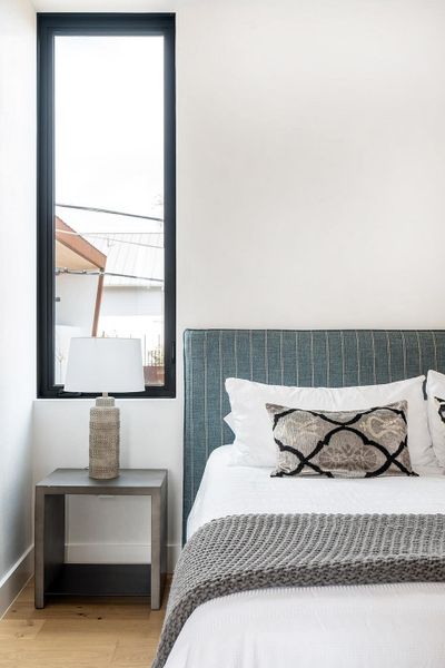 Hardwood flooring complements a bedroom's tall window and striped headboard. Hardwood flooring complements a bedroom's tall window and striped headboard.