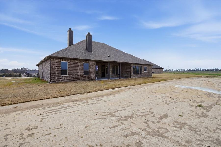 Rear view of property featuring a chimney, brick siding, a patio, and a lawn