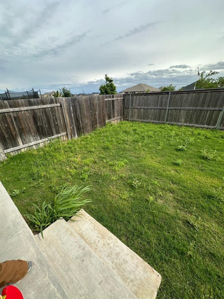The property features a fenced yard with a lawn and mature trees, offering privacy and a verdant outdoor space