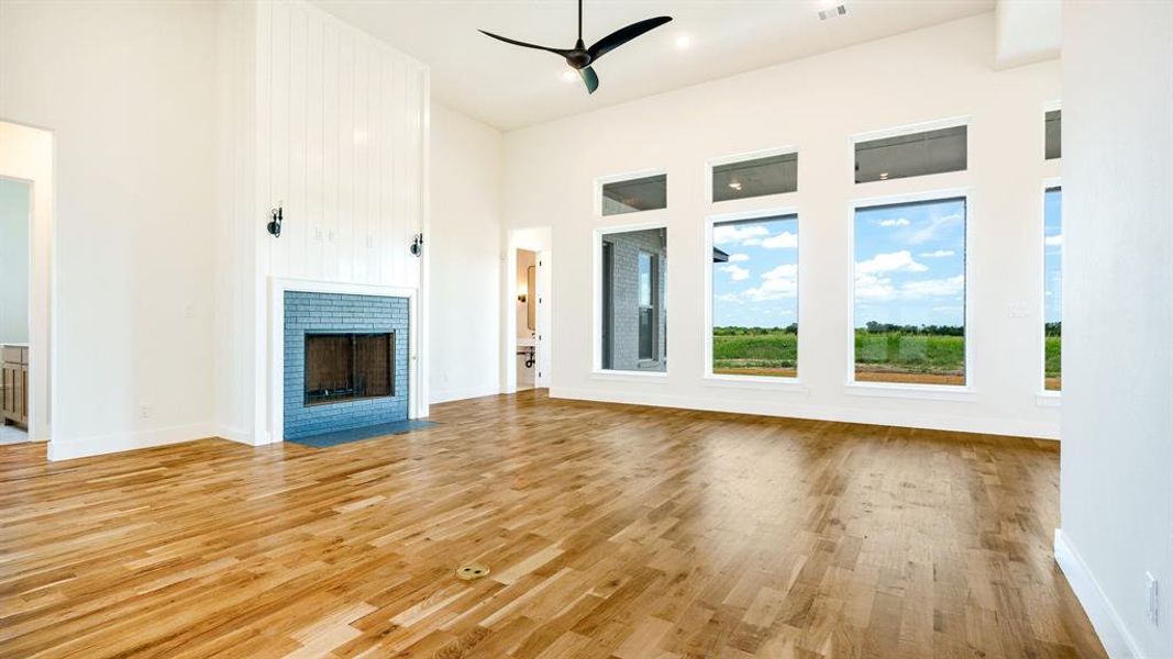 Unfurnished living room featuring light hardwood / wood-style floors, a high ceiling, a brick fireplace, and ceiling fan