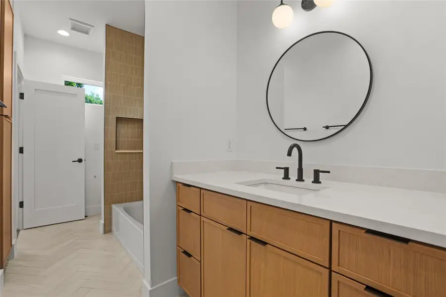 Clean lines define this bathroom, featuring a minimalist vanity with a sleek countertop and a modern circular mirror.